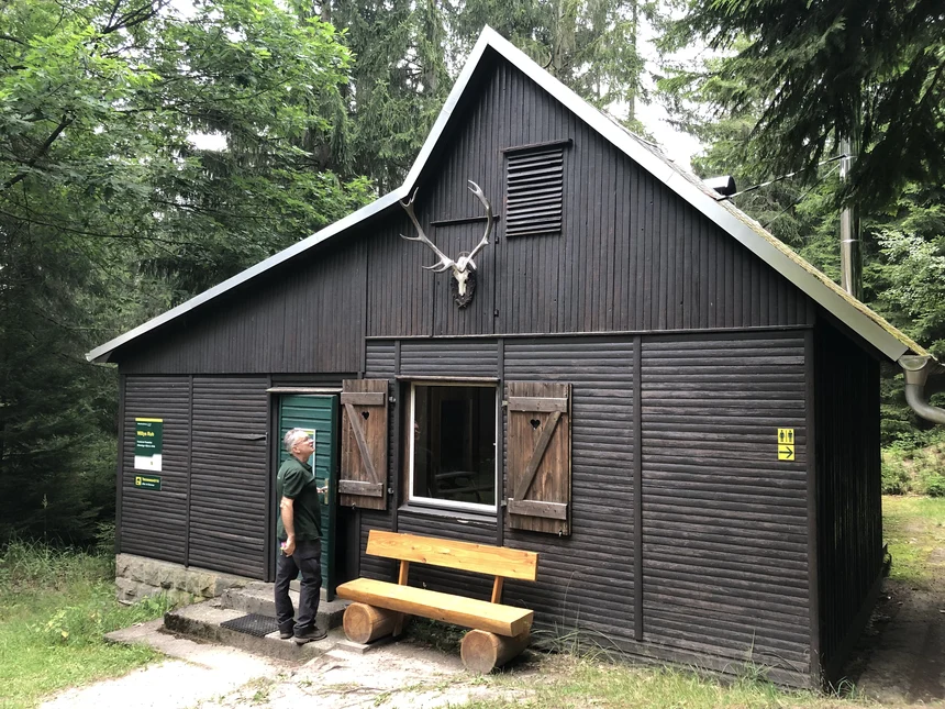Ein Mann steht an einer Hütte im Wald.