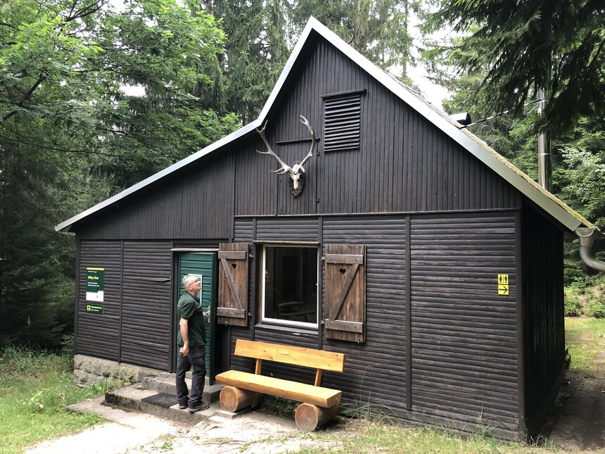 Ein Mann steht an einer Hütte im Wald.