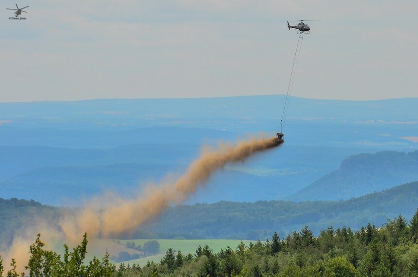 Hubschrauber über Wald wirft Kalkstaub ab