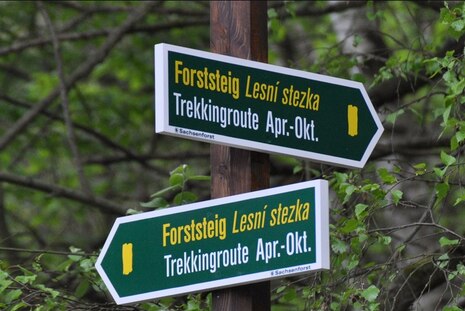 Mann im Vordergrund deutet mit einem Schlüssel in der Hand auf eine Trekkinghütte, die gerade von zwei Personen geputzt wird